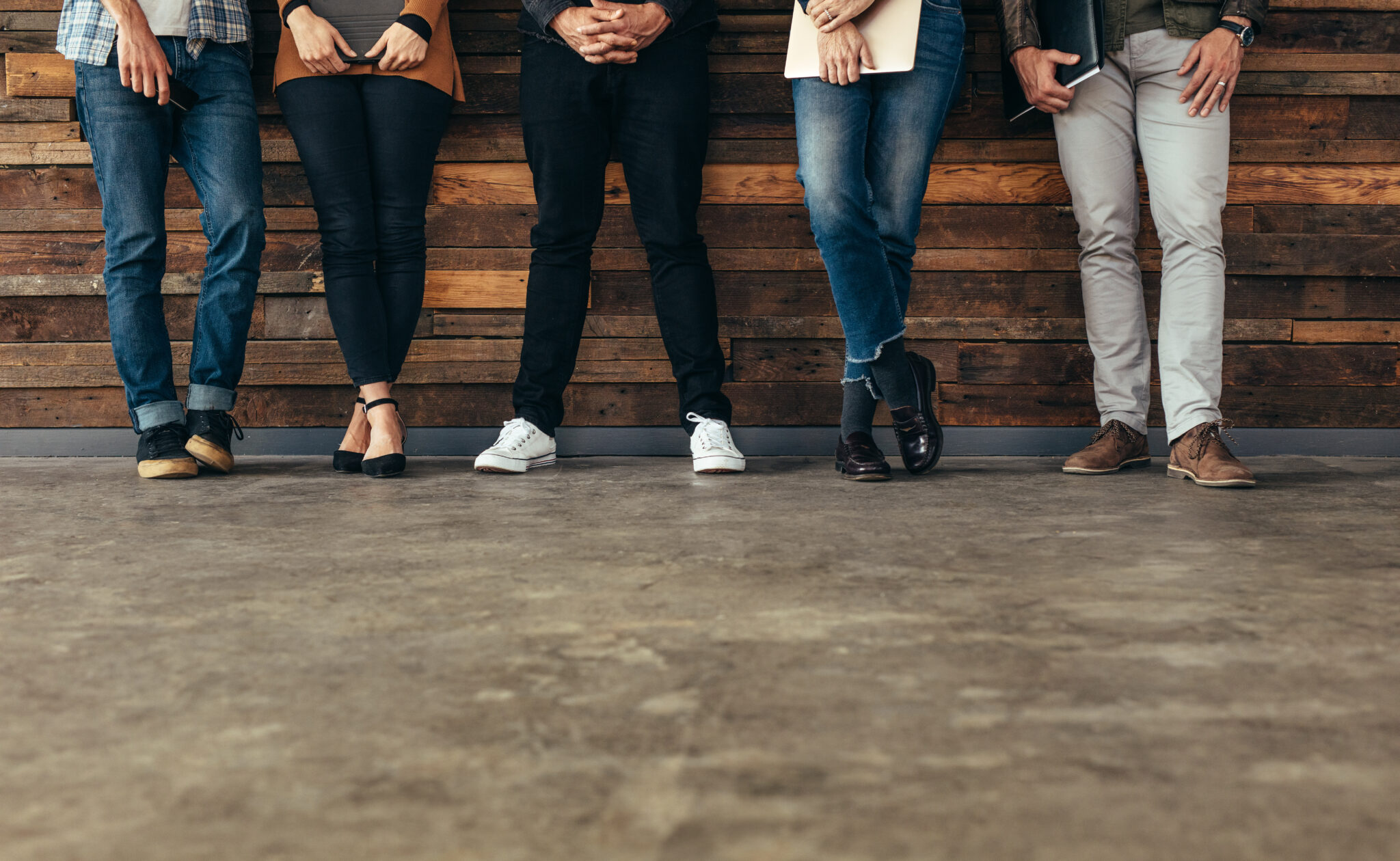 Group of people leaning against the wall before a job interview with folders in hands in the waiting room. Cropped shot of legs of people standing in row waiting for job interview.